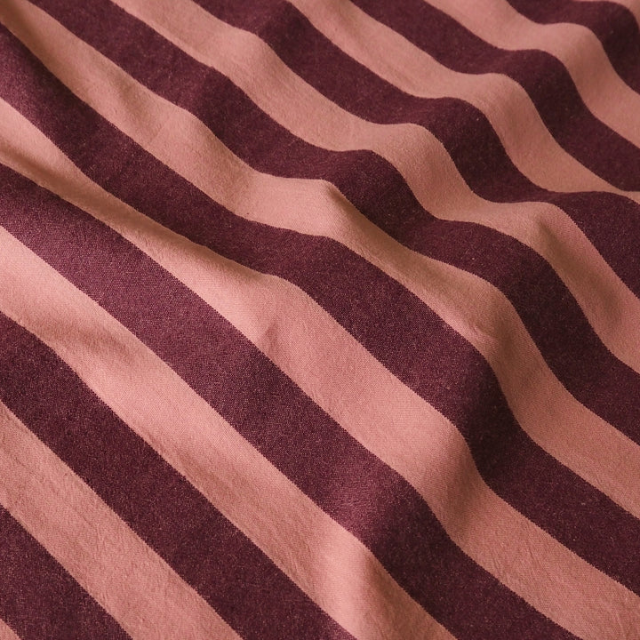 A close-up of a striped fabric with alternating wavy diagonal bands of dusty rose pink and deep burgundy.