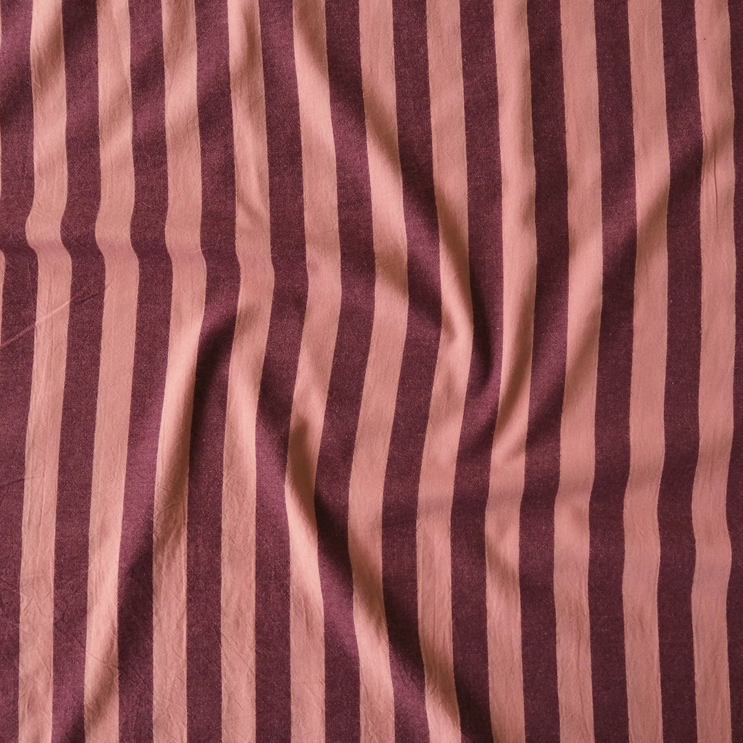 A close-up of a draped fabric with vertical stripes in dusty rose pink and deep burgundy.
