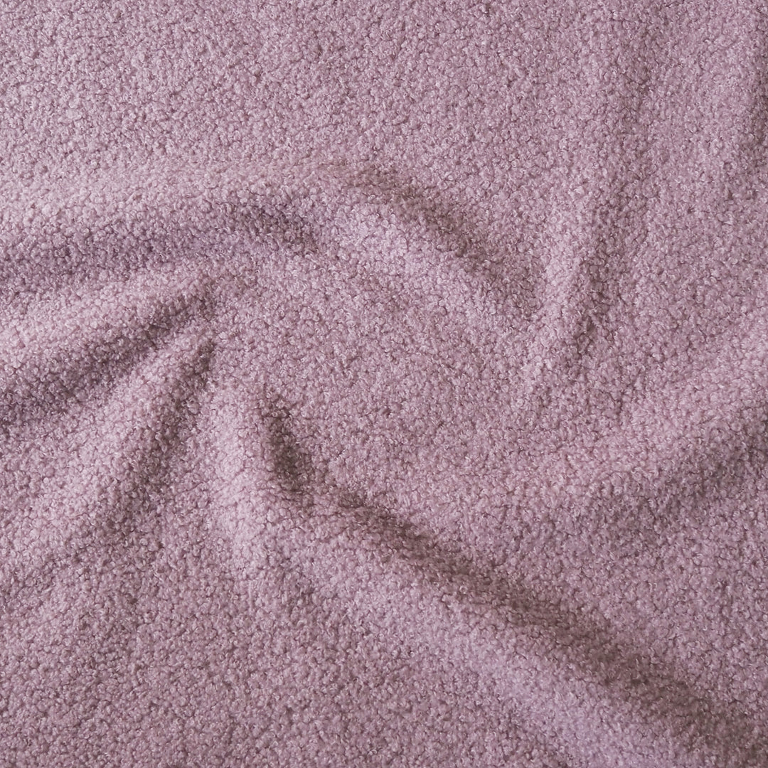 A close-up of textured fabric in a dusty mauve or muted lilac color, arranged with soft folds and swirls.