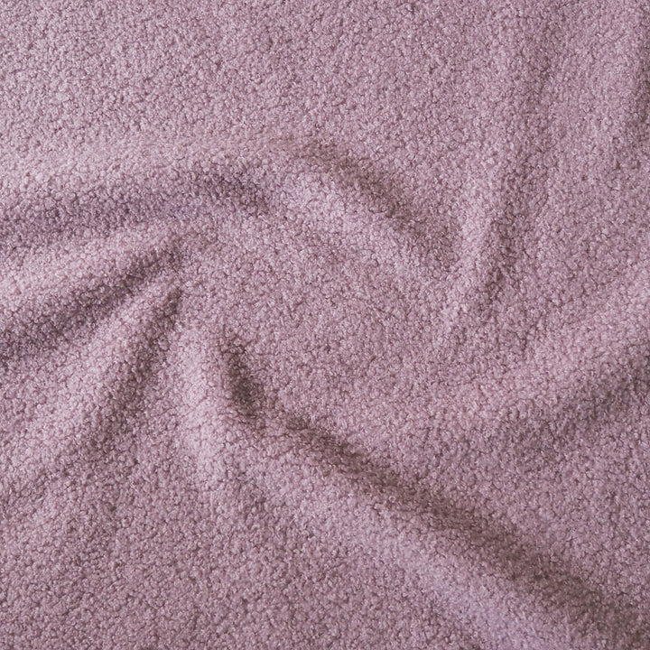 A close-up of textured fabric in a dusty mauve or muted lilac color, arranged with soft folds and swirls.