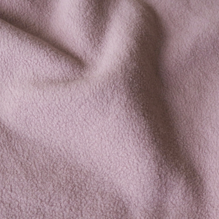 A close-up of soft, textured fabric in a dusty light pink color, showing gentle folds and a plush surface.