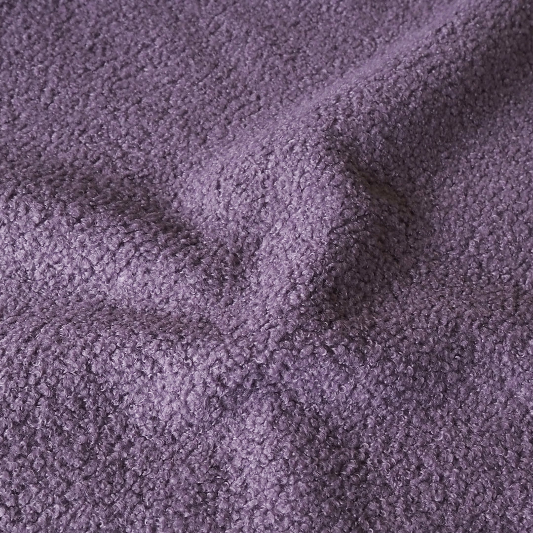A close-up of textured purple fabric with a soft, plush bouclé or sherpa-like surface, shown with gentle folds.