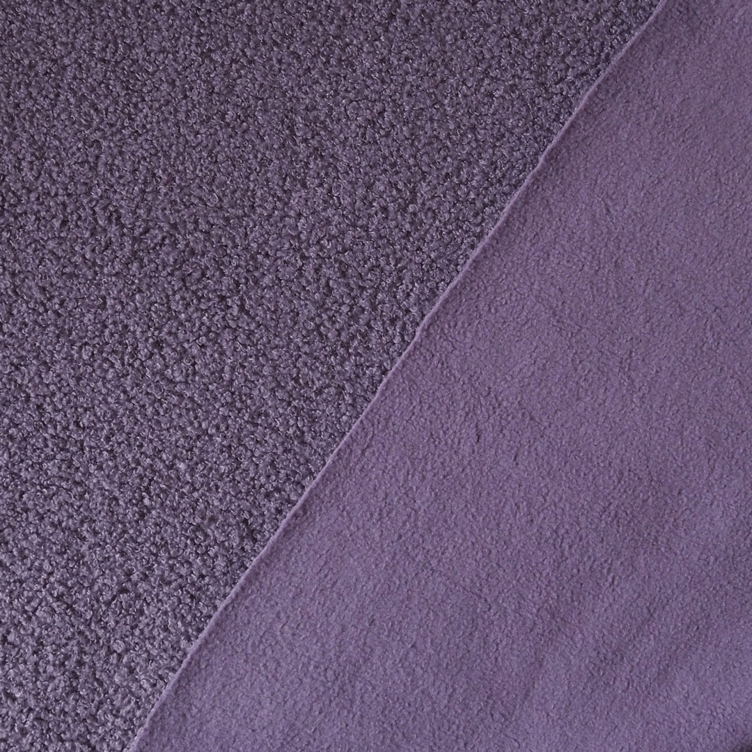 A close-up of a purple textured fabric, showing two different pile textures divided diagonally by a clean seam.