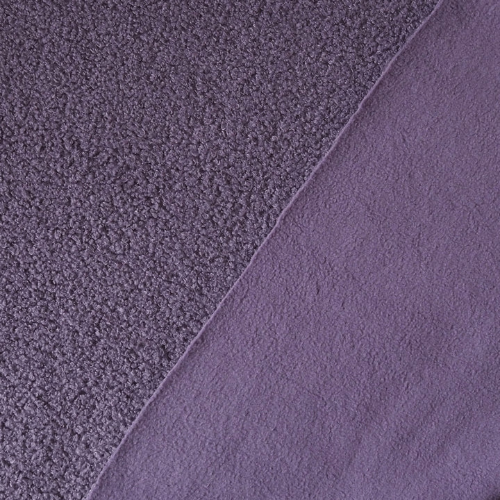 A close-up of a purple textured fabric, showing two different pile textures divided diagonally by a clean seam.