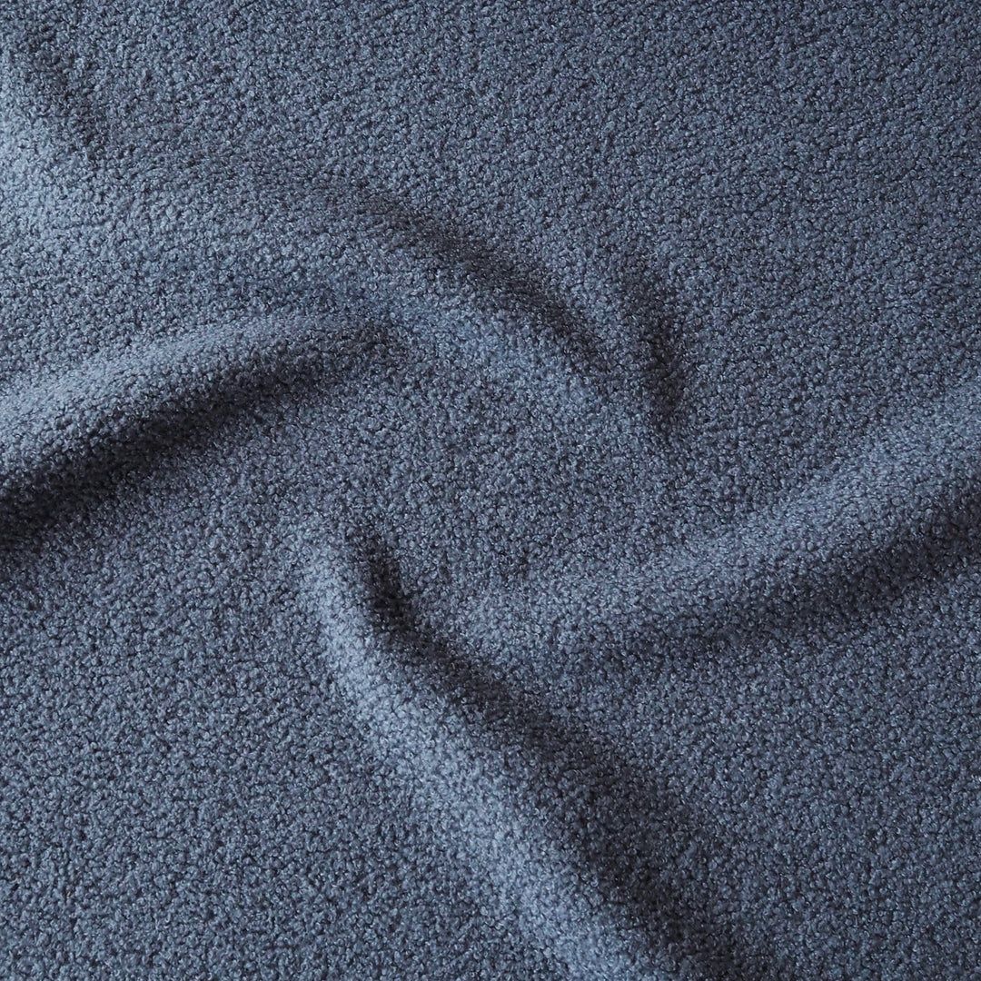 A close-up of textured fabric in a dark slate blue or navy color, arranged with soft folds that highlight its plush, looped surface.