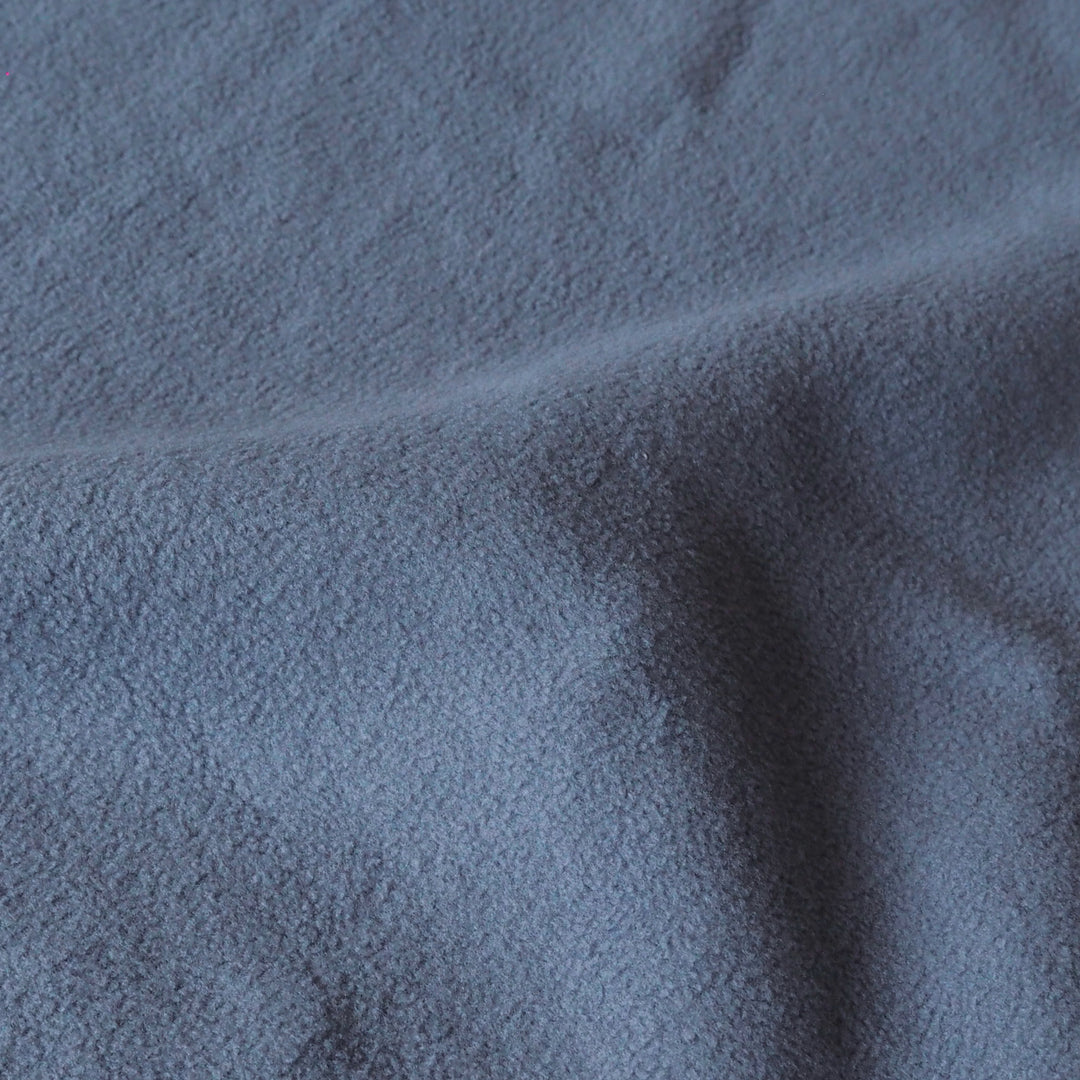 A close-up of a soft, textured fabric in a muted slate blue color, showing the material's fine weave and gentle folds.