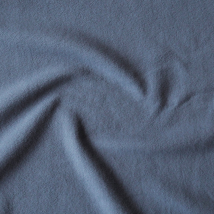 A close-up of textured fabric in a muted slate blue color, showing soft folds and a slightly nubby woven surface.