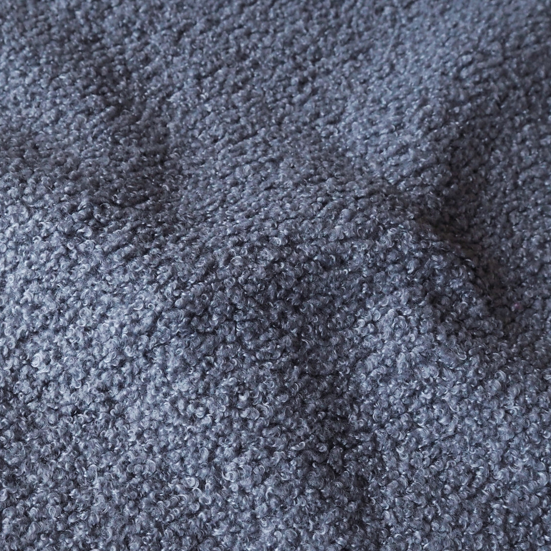 A close-up texture shot of a dark gray bouclé or sherpa fabric, showing the soft, nubby looped pile and subtle shadows in the folds.