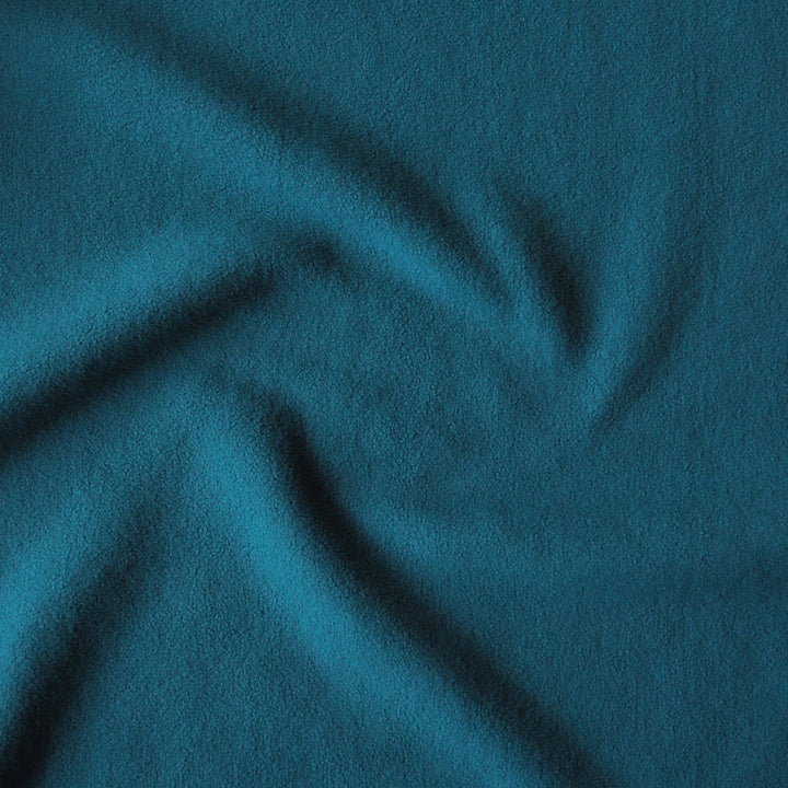 A close-up of textured fabric in a deep teal blue color, shown with soft folds and shadows.