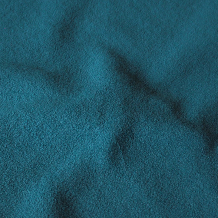 A close-up of textured fabric in a deep teal blue color, showing soft folds and a fine woven surface.