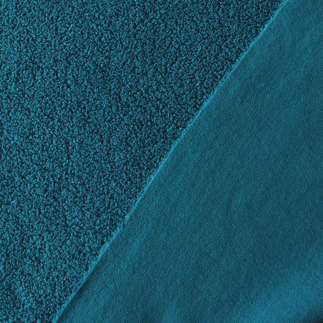 A close-up of teal fabric showing two different textures: a coarse, nubby bouclé texture on the left and a smoother, matte fabric on the right, divided by a diagonal seam.