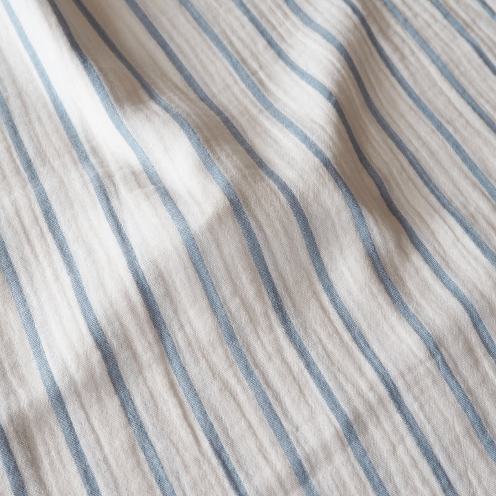 Close-up of a textured fabric with vertical blue stripes on a warm off-white background.