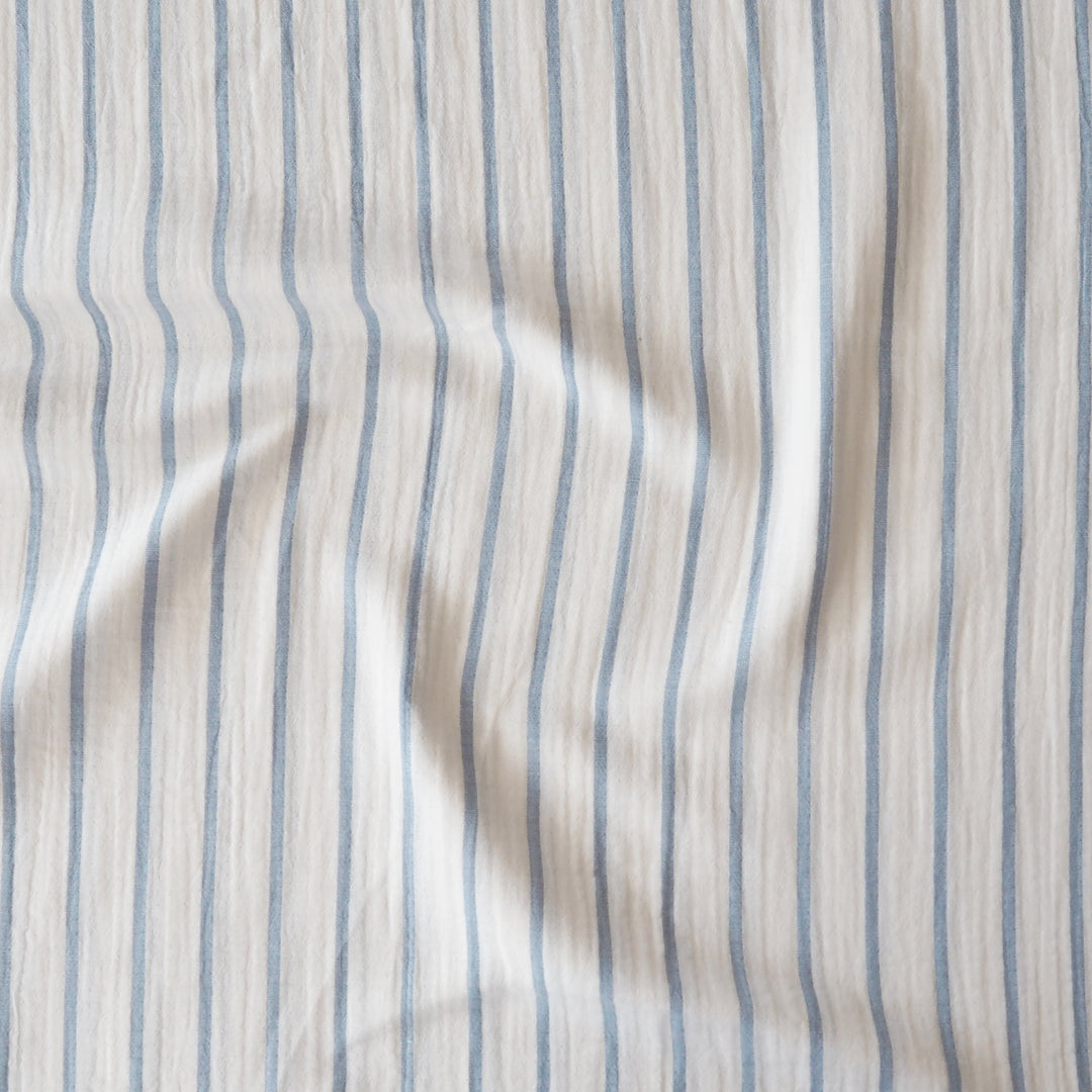 A close-up of a textured fabric with vertical light blue stripes on an off-white background.