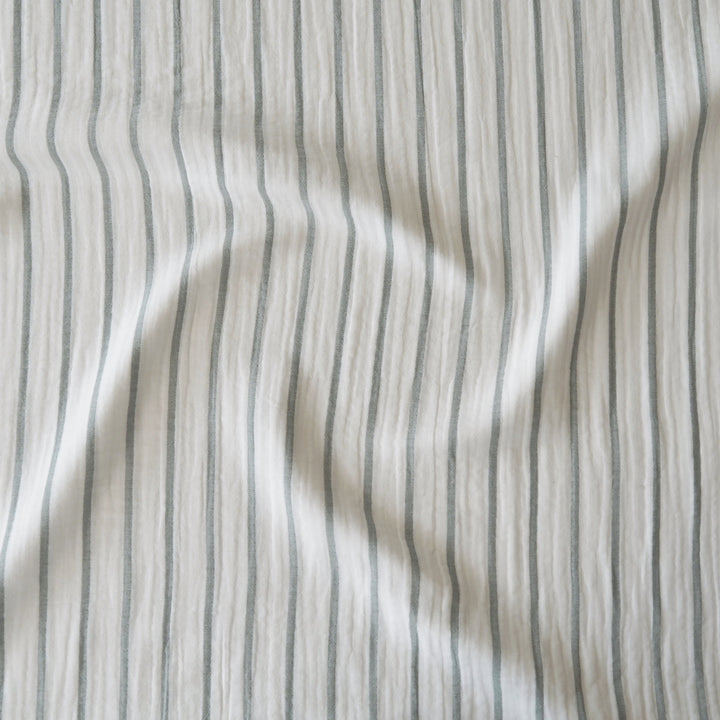 A close-up of a crinkled fabric with vertical stripes in muted gray on an off-white background.