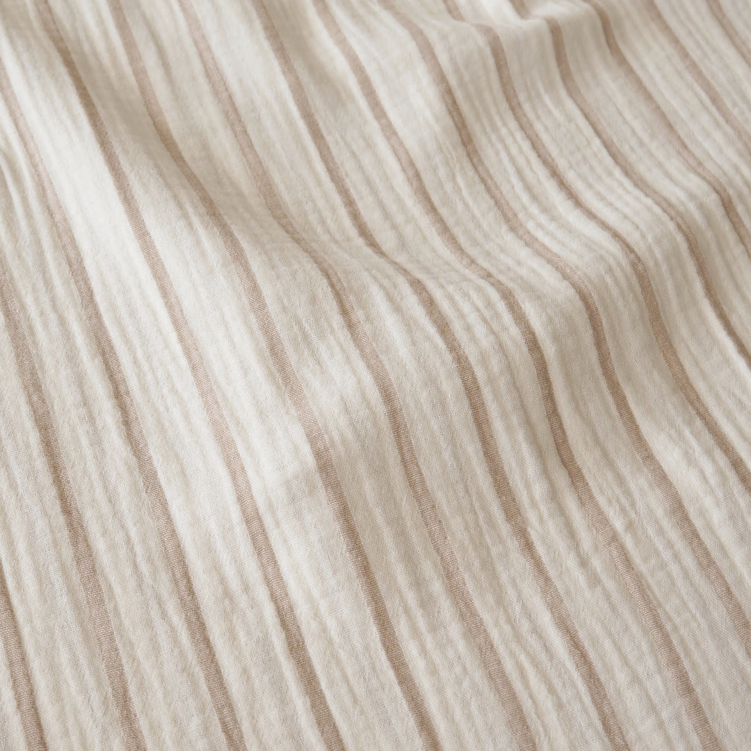 A close-up of a textured, crinkled fabric with vertical stripes in warm beige and cream.