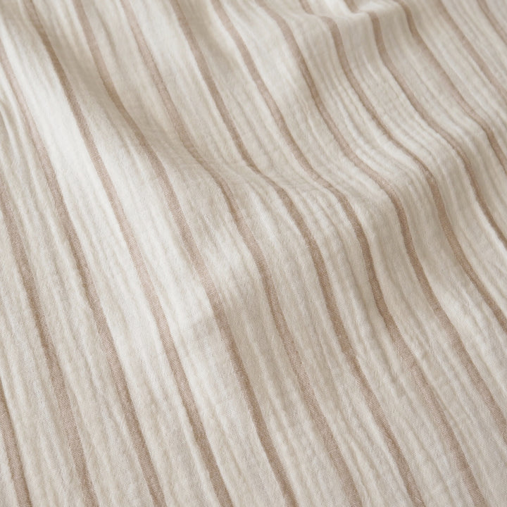 A close-up of a textured, crinkled fabric with vertical stripes in warm beige and cream.