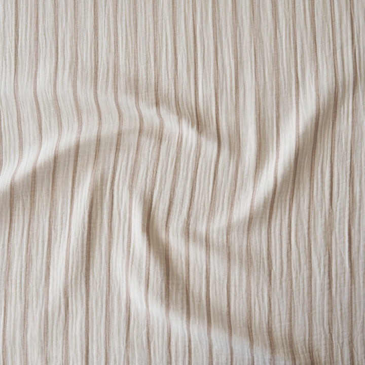 A close-up of a textured fabric with vertical beige and cream stripes, showing a soft crinkled or gauze-like surface with gentle folds.