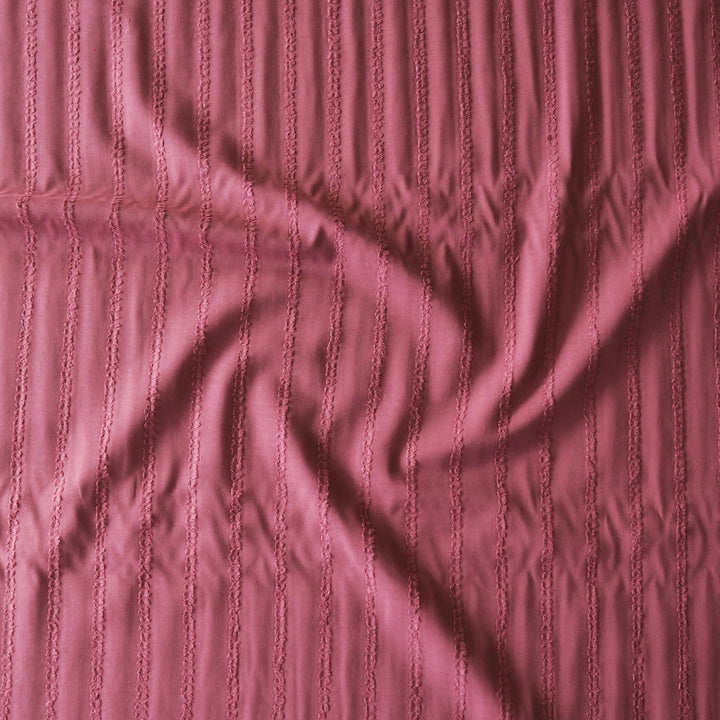 A close-up of a dusty rose pink fabric with a vertical textured stripe pattern, shown with soft folds and shadows.