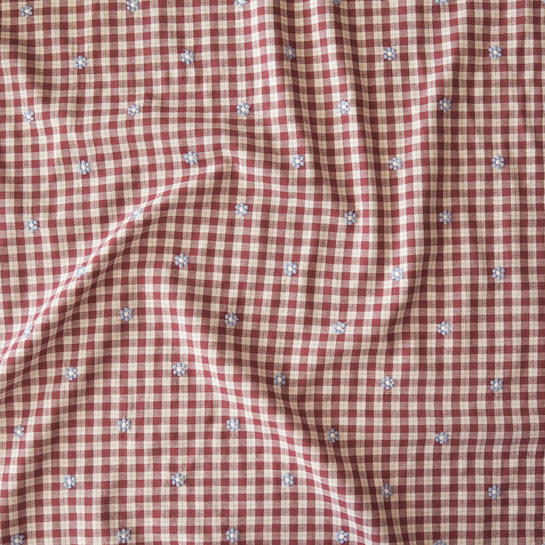 A close-up of a red and white gingham fabric with small embroidered floral details scattered throughout.