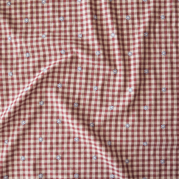A close-up of a red and white gingham fabric with small embroidered floral details scattered throughout.