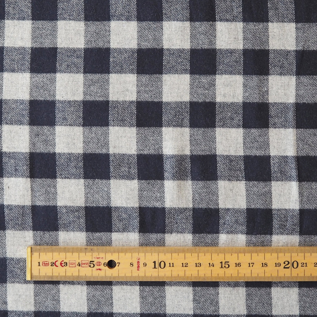A close-up of a navy blue and light gray gingham fabric pattern with a wooden ruler along the bottom edge for scale.