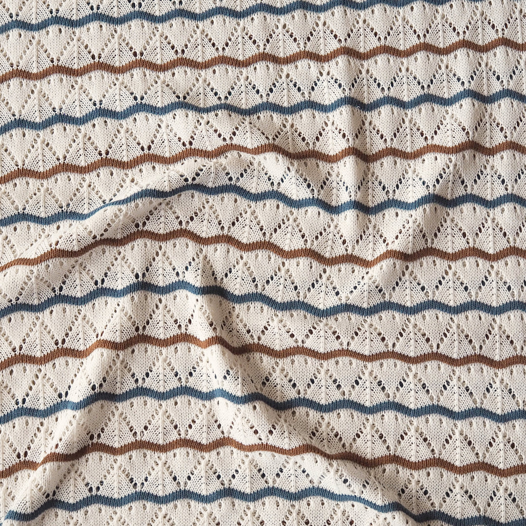 Close-up of a textured knit fabric with a cream base and horizontal wavy stripes in blue and brown, featuring an openwork diamond pattern.