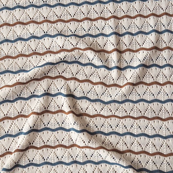 Close-up of a textured knit fabric with a cream base and horizontal wavy stripes in blue and brown, featuring an openwork diamond pattern.