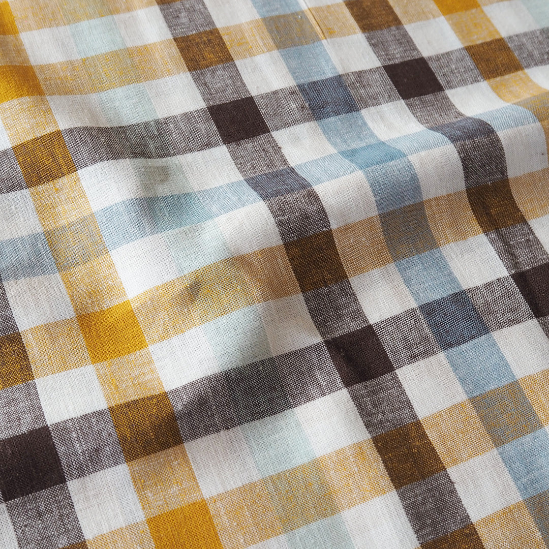 A close-up of a plaid fabric with a textured linen-like weave, featuring intersecting stripes of mustard yellow, brown, slate blue, charcoal gray, and off-white.