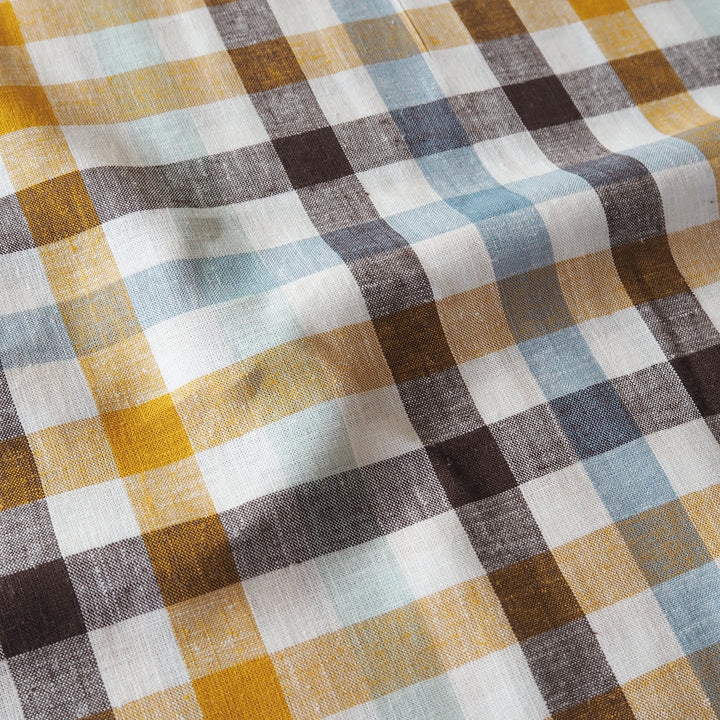 A close-up of a plaid fabric with a textured linen-like weave, featuring intersecting stripes of mustard yellow, brown, slate blue, charcoal gray, and off-white.