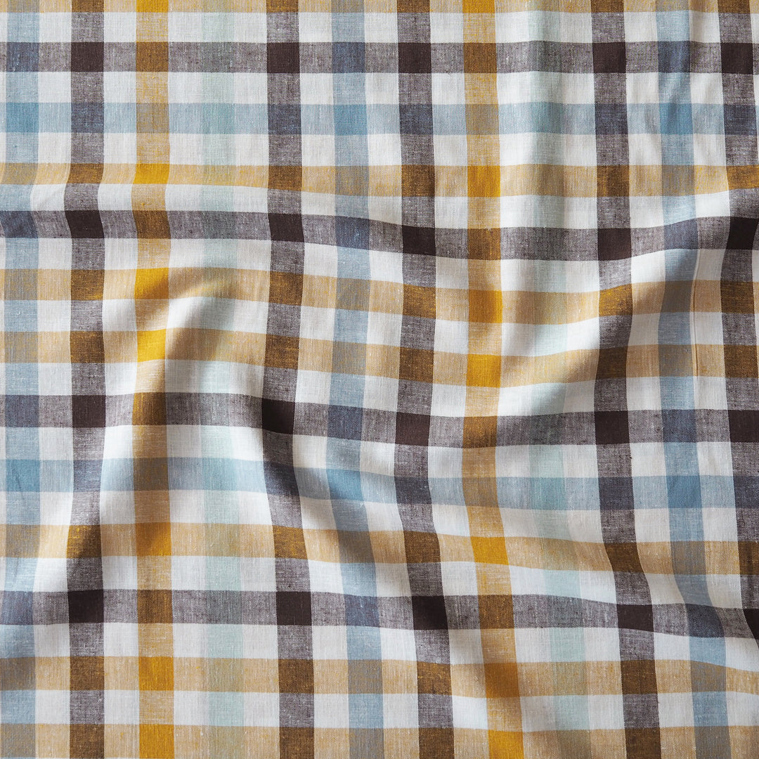 A close-up of a plaid fabric pattern with white, mustard yellow, light blue, and dark brown stripes in a gingham check design.