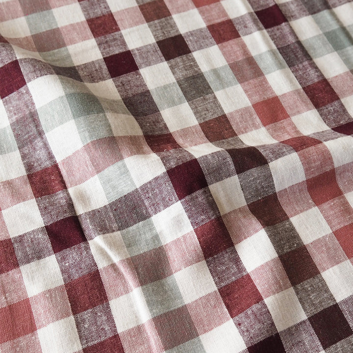 A close-up of a plaid fabric with a textured weave, featuring intersecting stripes of burgundy red, dusty rose, dark brown, and off-white.