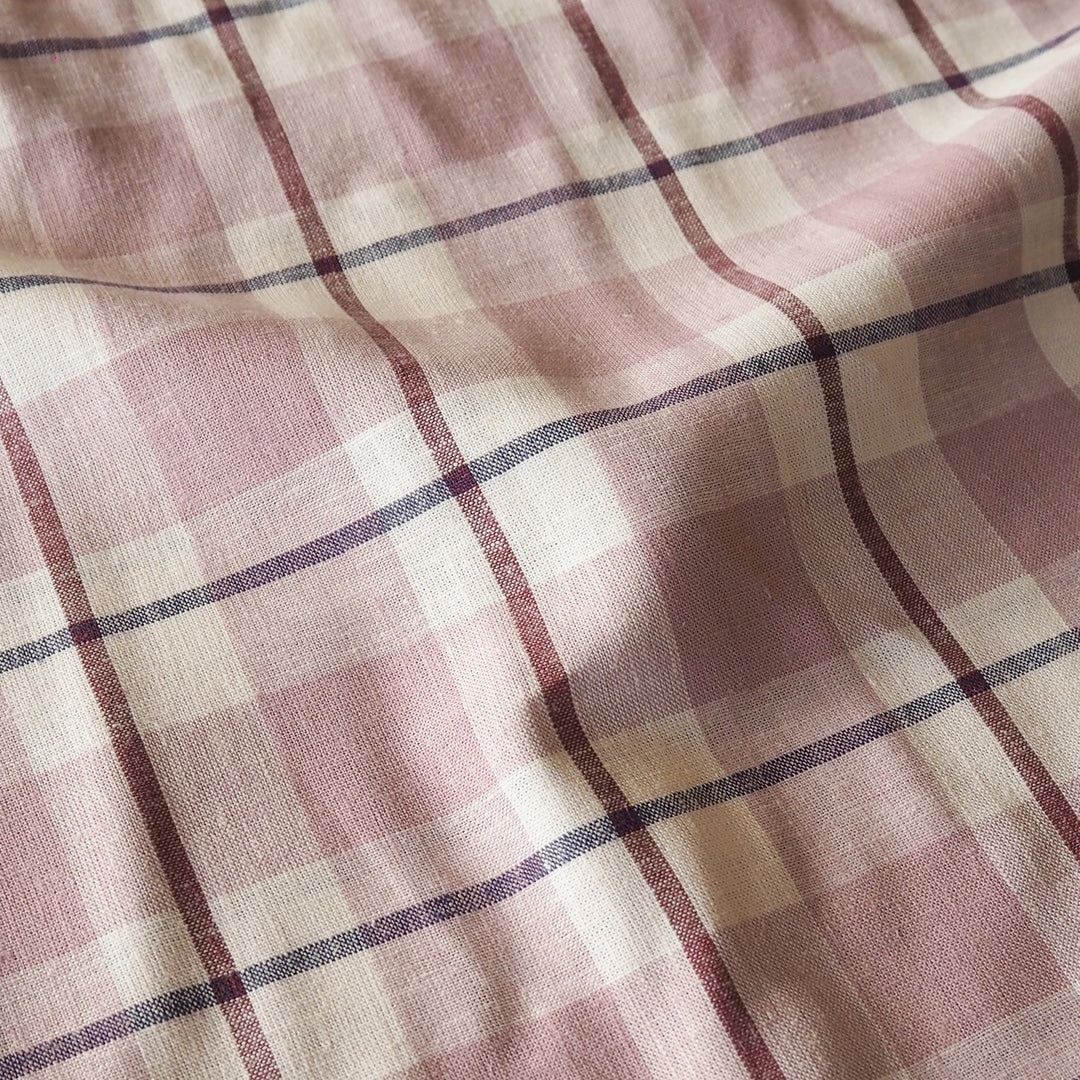 A close-up of a plaid fabric with a dusty pink and cream checkered pattern, accented by thin dark purple lines.