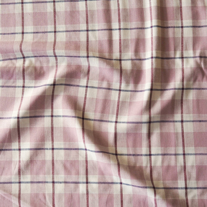 Pink and off-white plaid fabric with thin dark purple stripes, shown with soft folds and wrinkles.