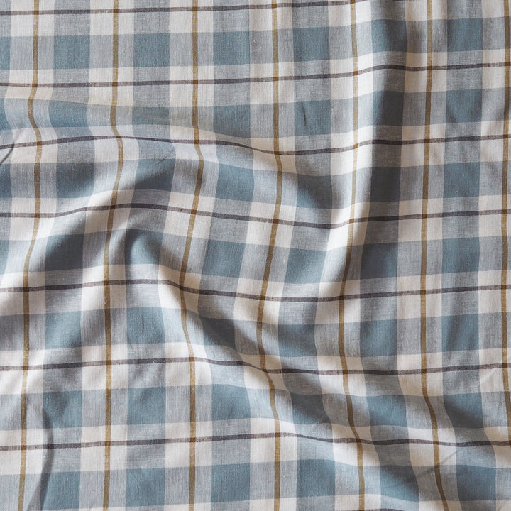 A close-up of a plaid fabric with a light blue, white, and tan checkered pattern, showing soft folds and wrinkles.