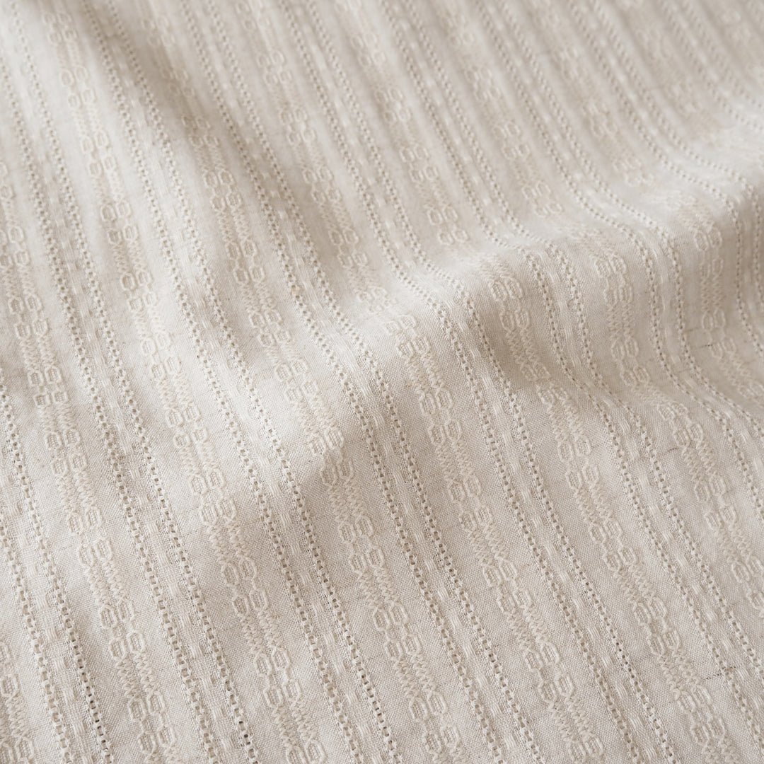 A close-up of a textured cream-colored fabric with a fine vertical eyelet or embroidered stripe pattern.