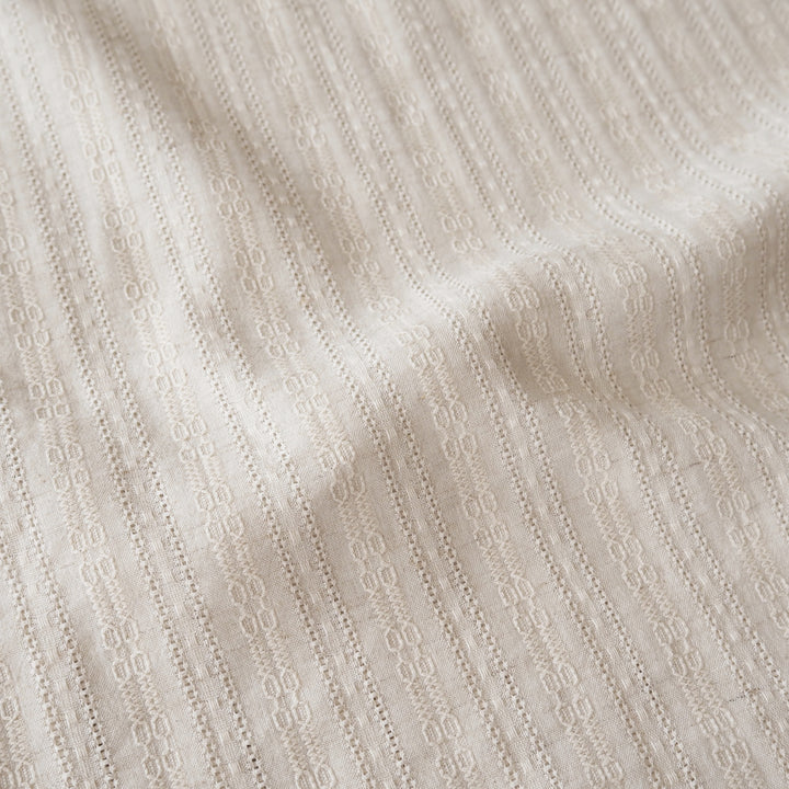 A close-up of a textured cream-colored fabric with a fine vertical eyelet or embroidered stripe pattern.