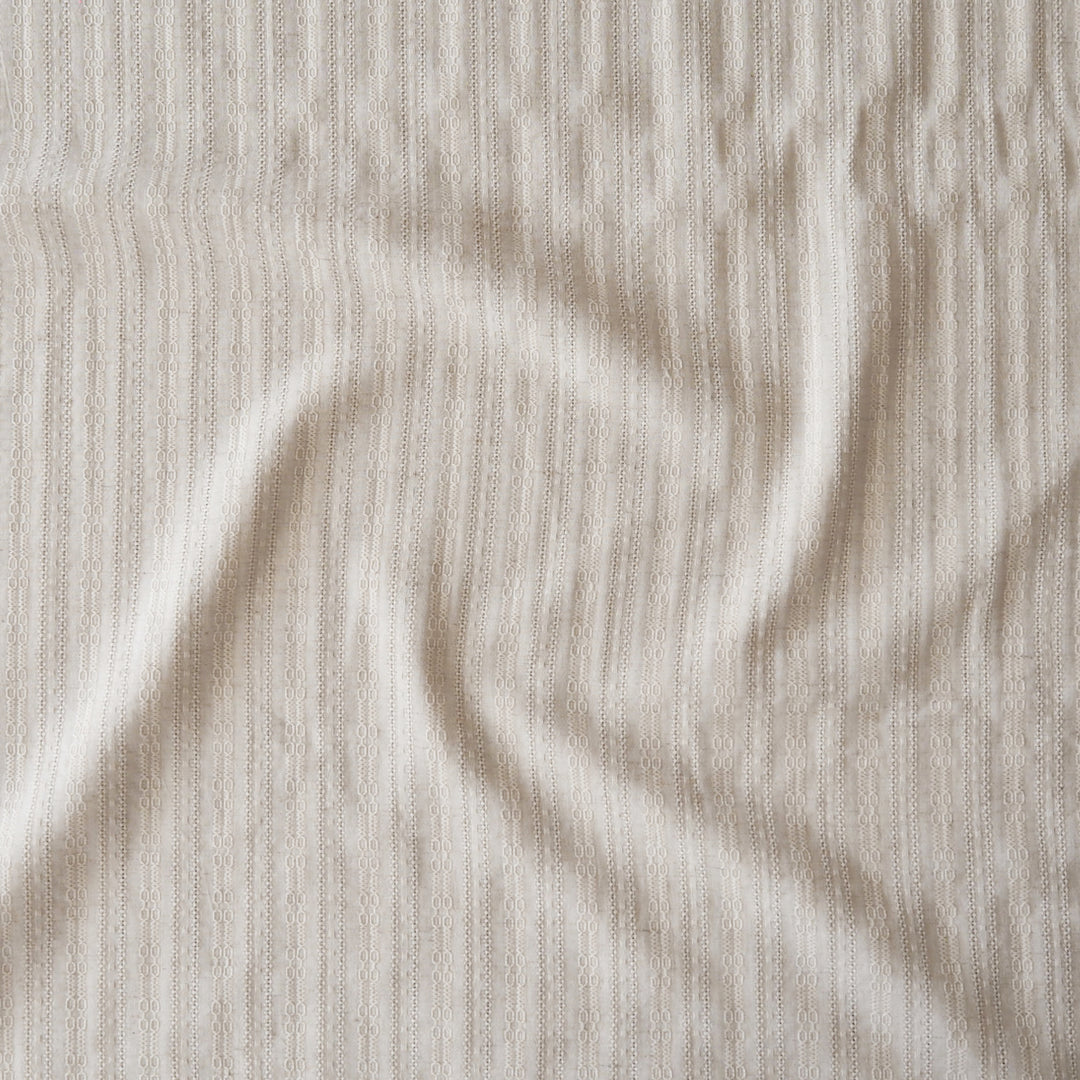 A close-up of a textured, ribbed fabric in a warm off-white or cream color, shown with soft folds and shadows.