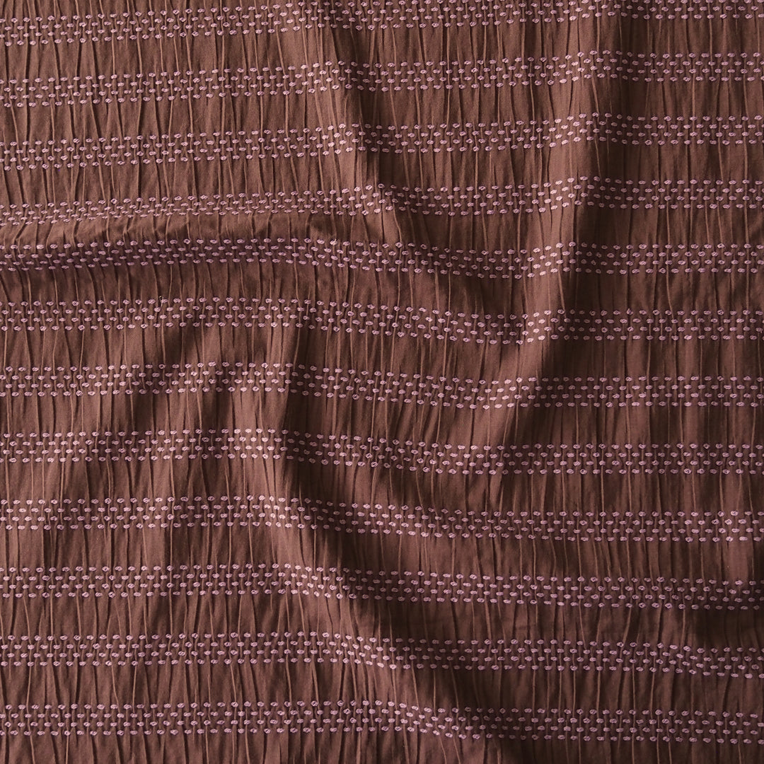 A close-up of a brown fabric with horizontal gathered stripes and small woven geometric details.