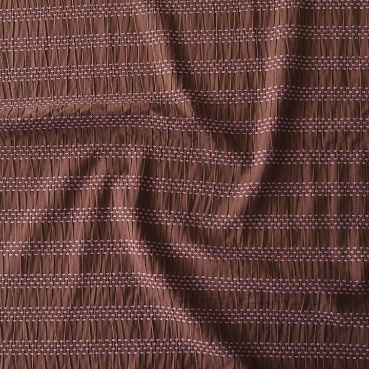 A close-up of a brown fabric with horizontal gathered stripes and small woven geometric details.