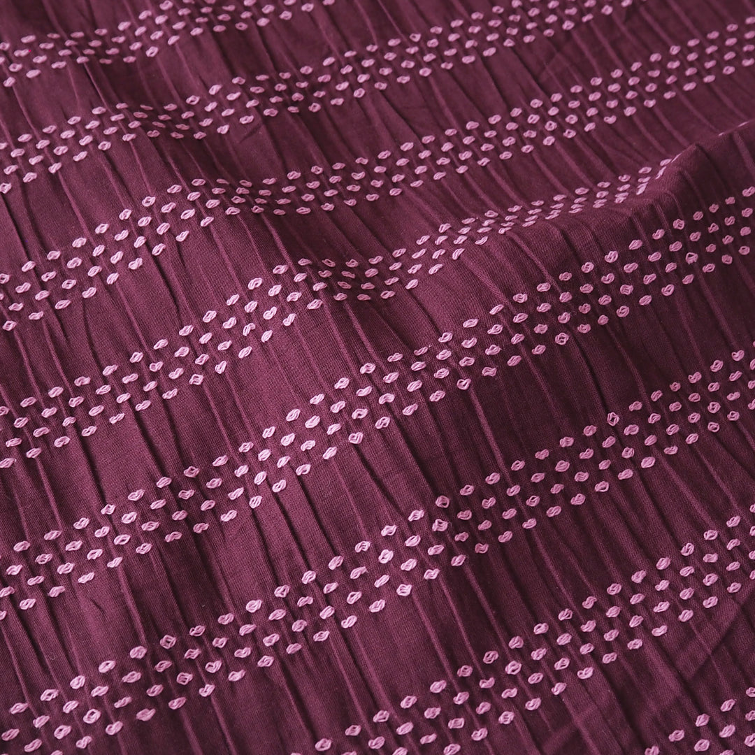 A close-up of a pleated fabric in a deep plum purple color, decorated with horizontal rows of small light pink embroidered dots.