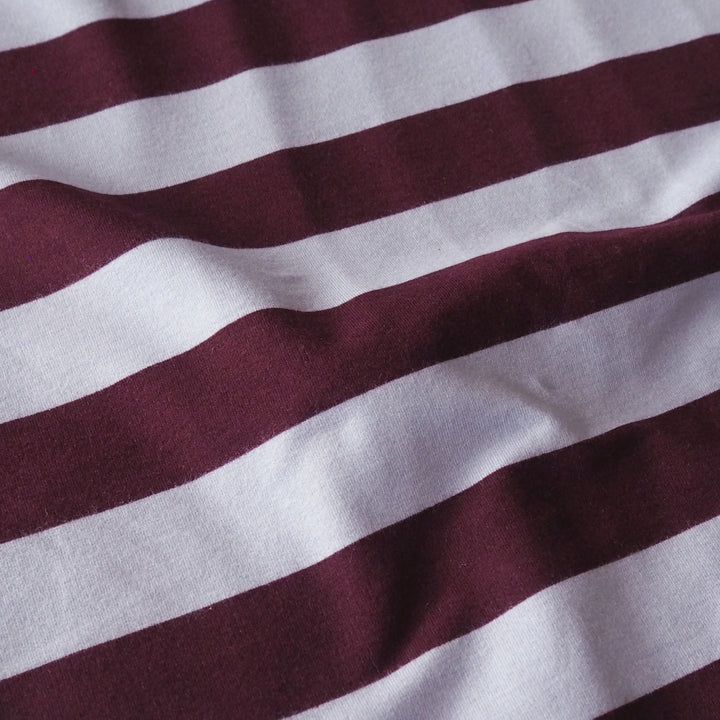 A close-up of a striped fabric with alternating wide and narrow horizontal stripes in deep burgundy and white, showing soft folds and a textured weave.
