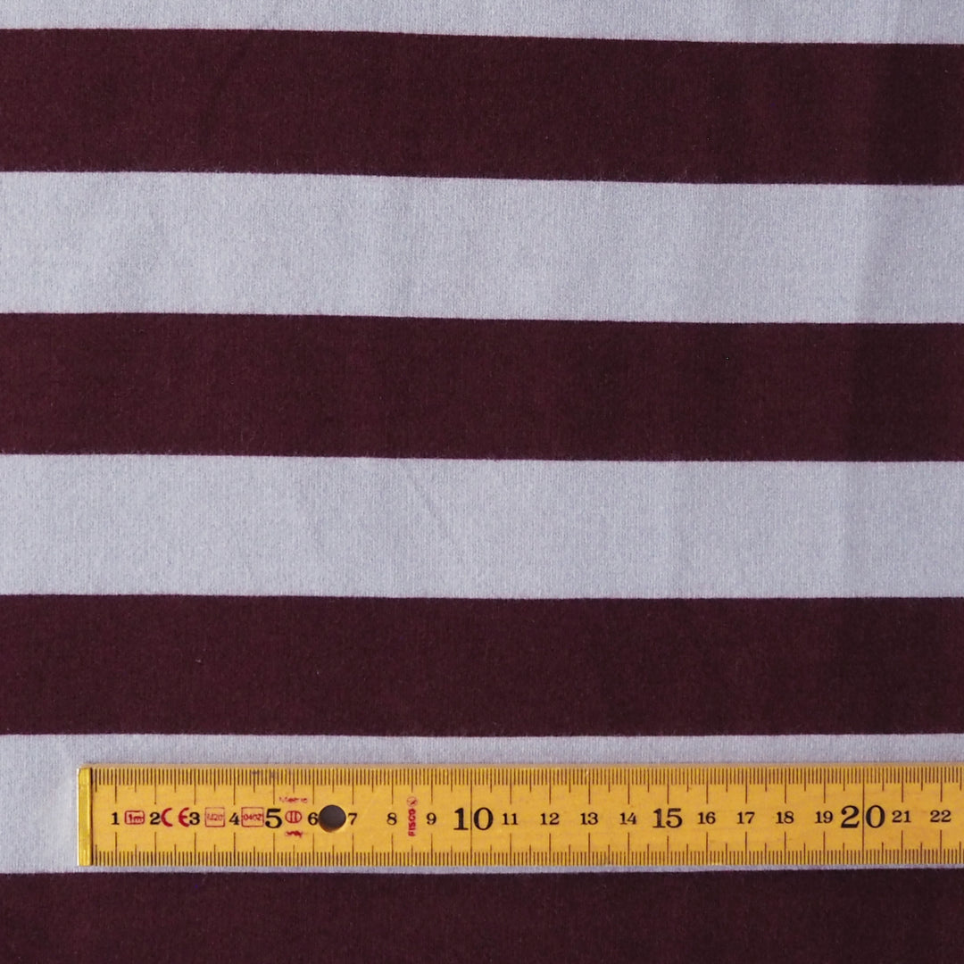 A close-up of a striped fabric with alternating dark burgundy and light gray horizontal bands, with a yellow measuring tape ruler laid along the bottom edge for scale.