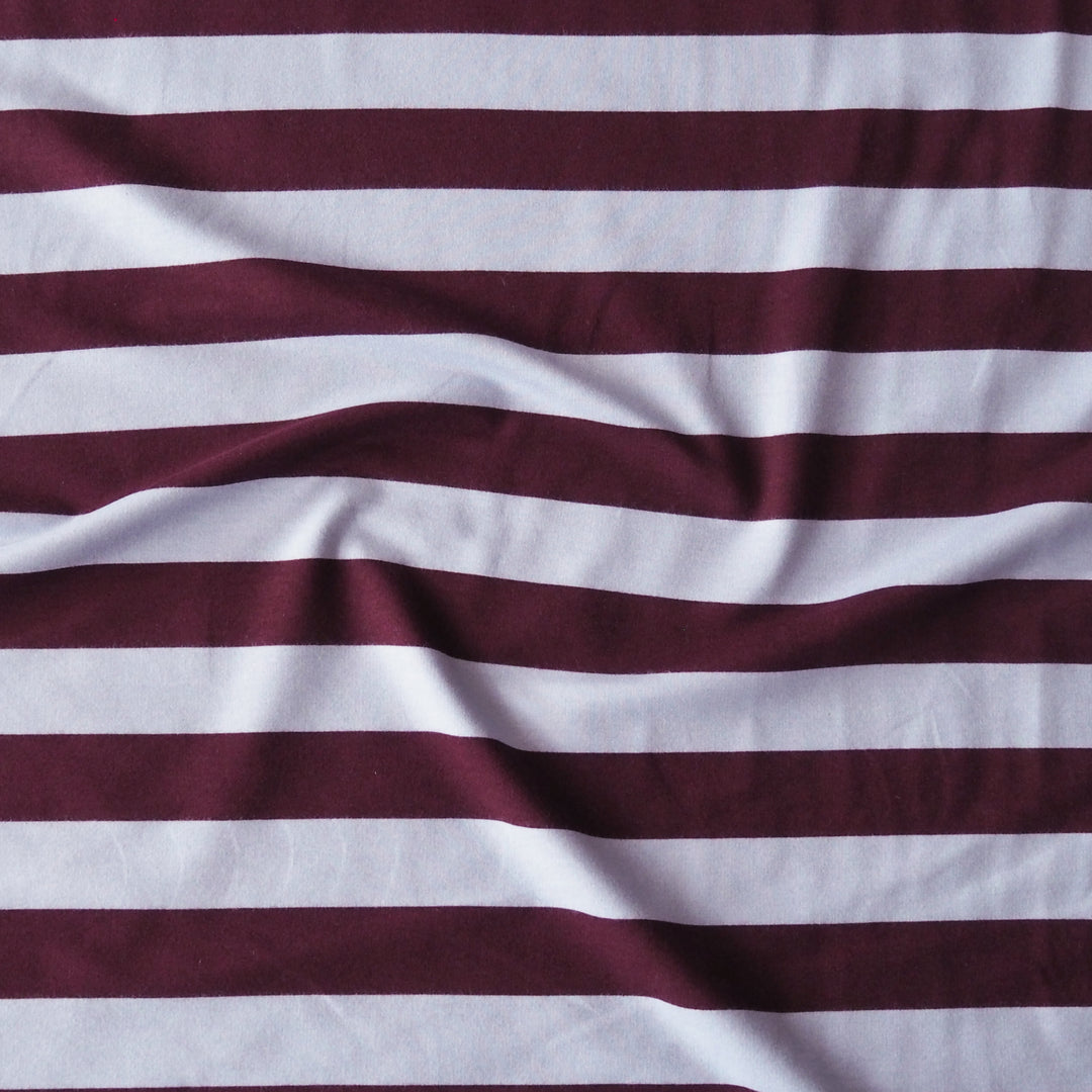 A close-up of a striped fabric with alternating horizontal bands of deep burgundy and white, showing soft folds and a textured weave.