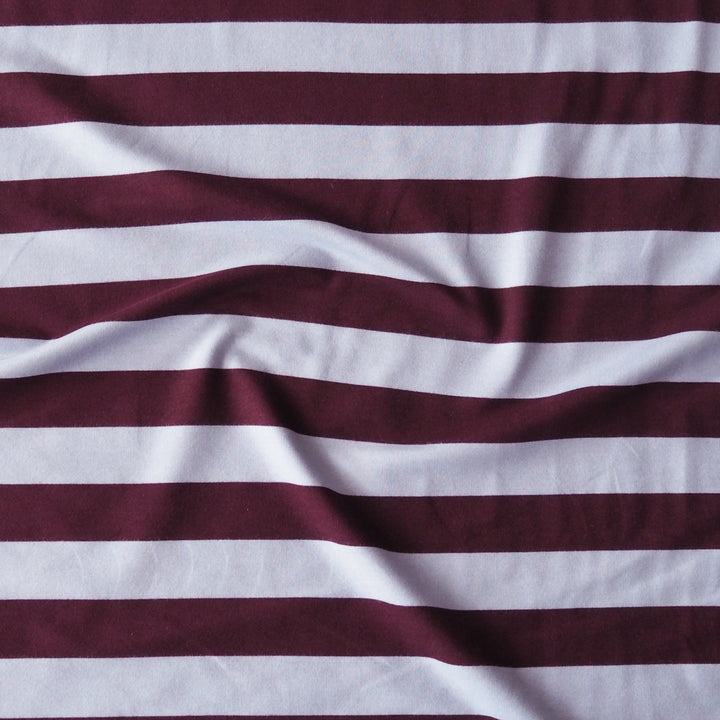 A close-up of a striped fabric with alternating horizontal bands of deep burgundy and white, showing soft folds and a textured weave.