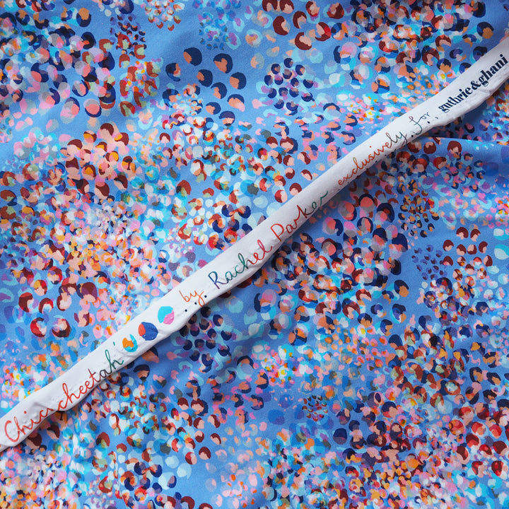 A close-up of a white fabric selvedge laid diagonally across a blue and multicolor patterned fabric. 