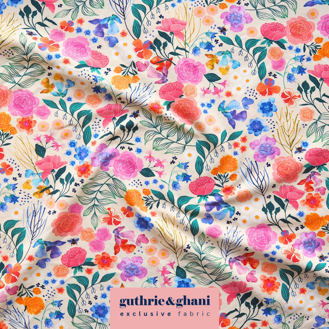A close-up of a draped fabric featuring a vibrant watercolor floral print on a cream background. The pattern includes pink, orange, blue, and purple flowers with green and teal leaves.