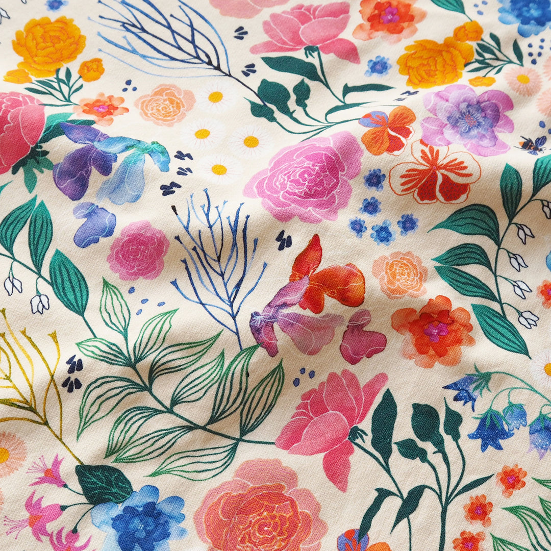 A close-up of a floral fabric pattern on a cream-colored background, featuring watercolor-style flowers in pink, orange, blue, purple, and green with delicate leafy stems.