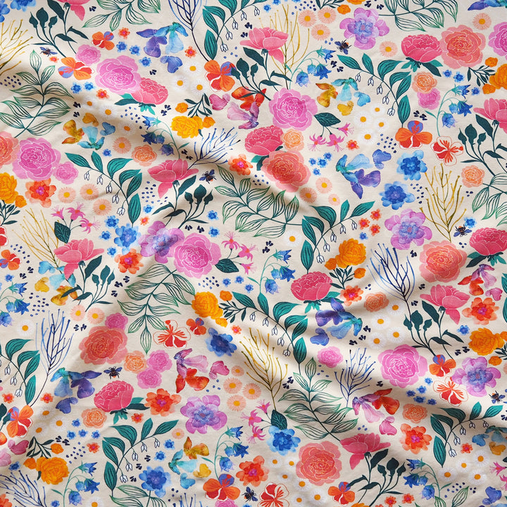 A close-up of a draped fabric featuring a vibrant, multicolor floral print on a warm cream background. The pattern includes pink, orange, blue, purple, and green watercolor-style flowers and leaves.