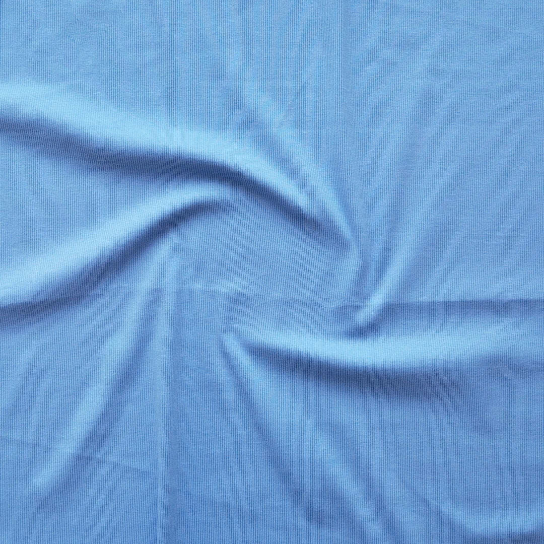 A close-up of light blue fabric with a subtle woven texture, arranged with soft swirls and folds.