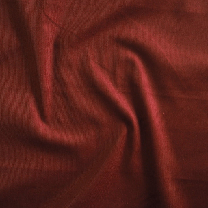 Dark amber stretch cotton needlecord fabric, fine cord texture.